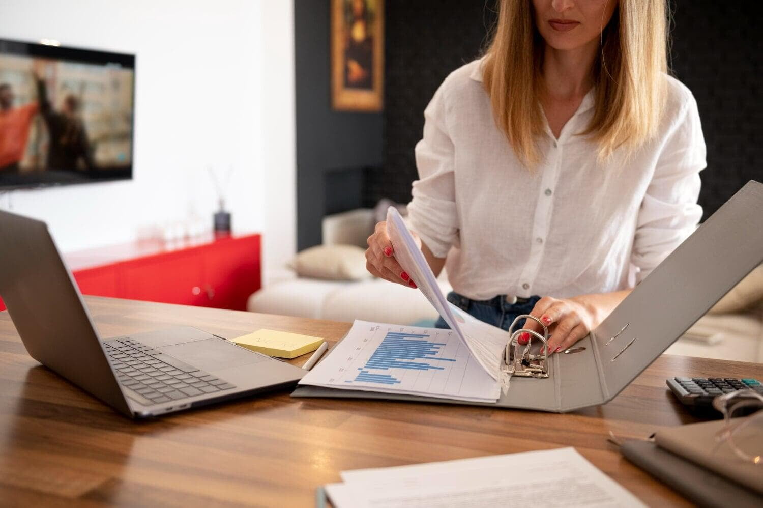 Mulher sentada em mesa com notebook abrindo pasta com relatórios