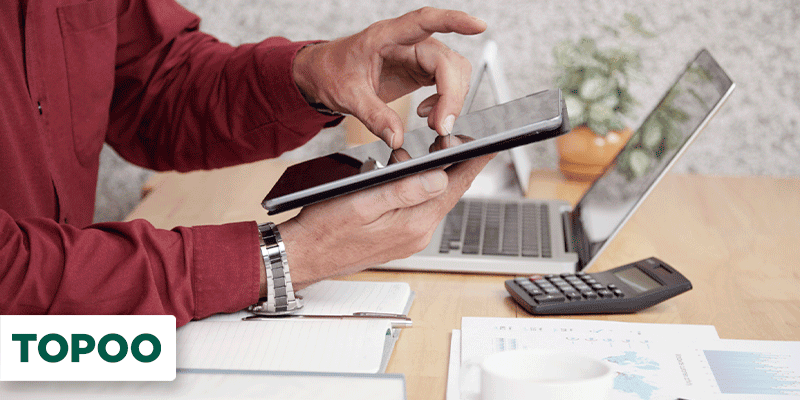 Homem mexendo em tablet numa mesa com notebook, calculadora e papéis