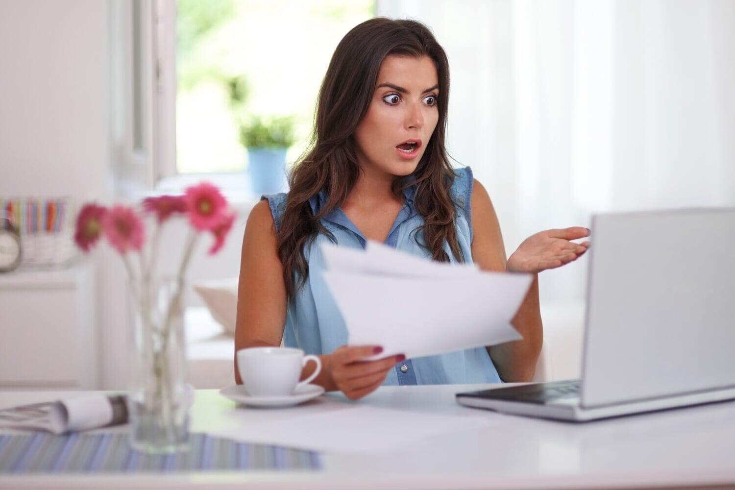 Mulher segurando papéis espantada olhando para notebook